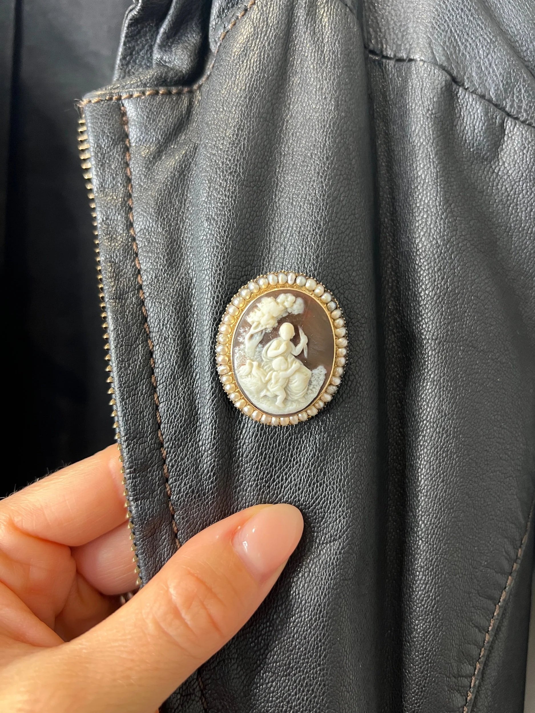 An antique oval cameo brooch depicting cherubs and birds, with a pearl border, set in gold, on a black jacket
