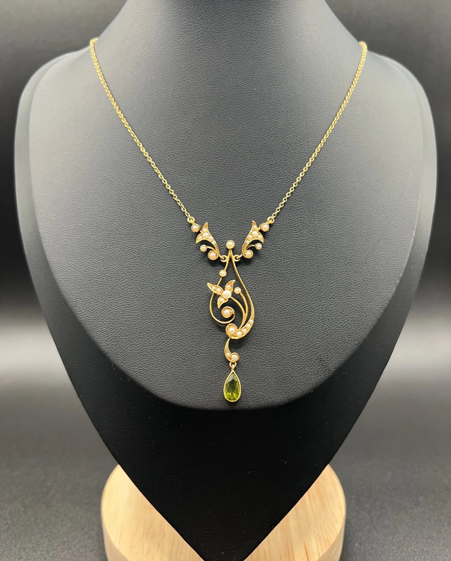 A yellow gold floral pendant necklace with pearls and a peridot drop, on a black jewellery bust
