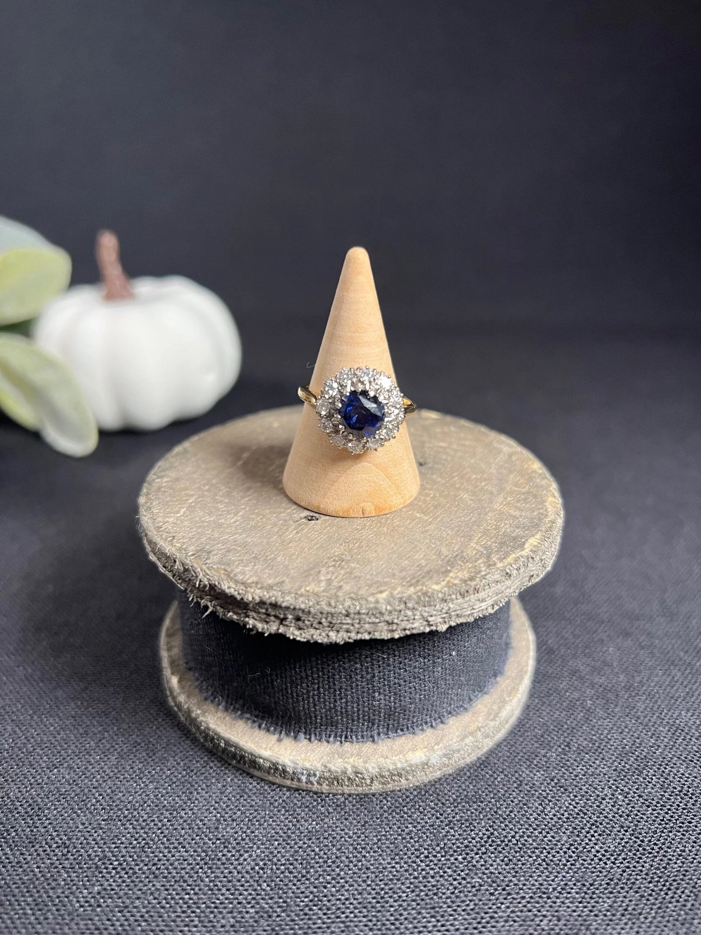 A round sapphire and diamond cluster ring, on a wooden ring cone