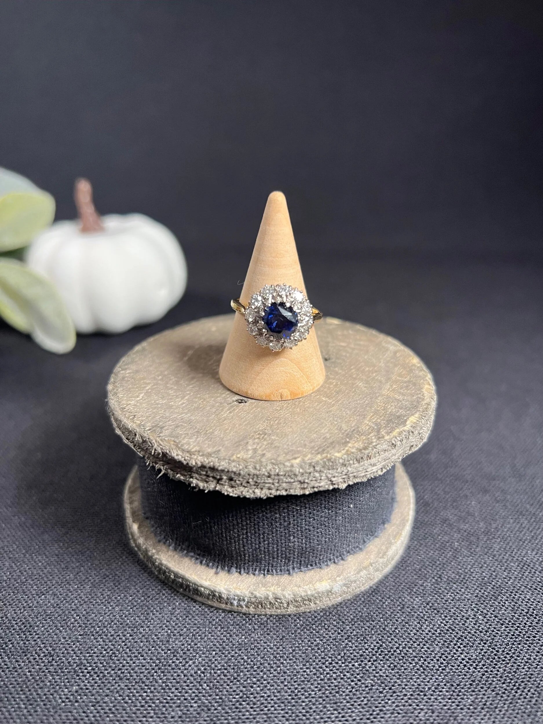 A round sapphire and diamond cluster ring, on a wooden ring cone