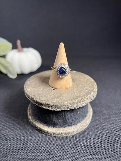 A round sapphire and diamond cluster ring, on a wooden ring cone