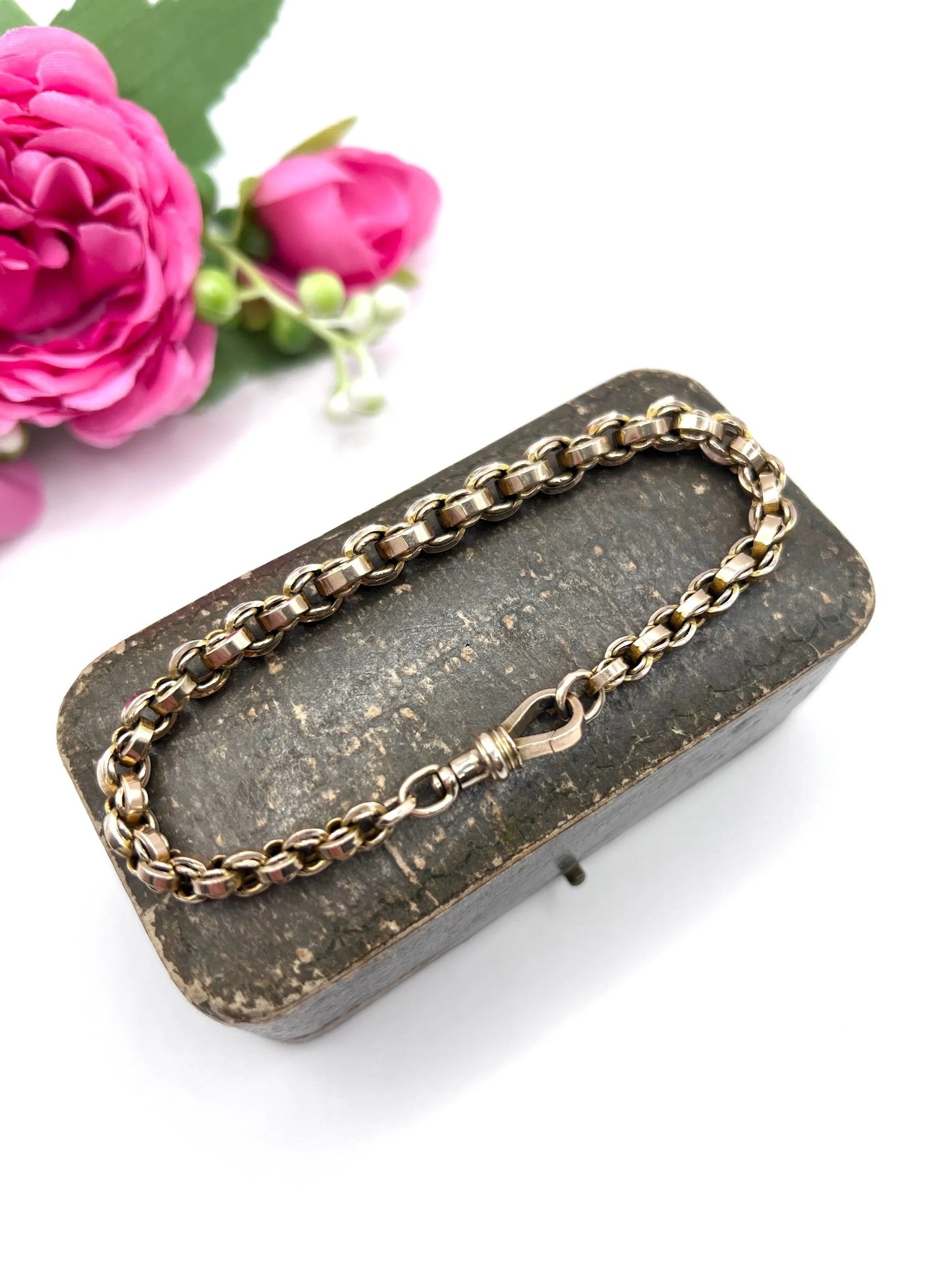 A gold round link bracelet with a lobster claw clasp, on an antique box