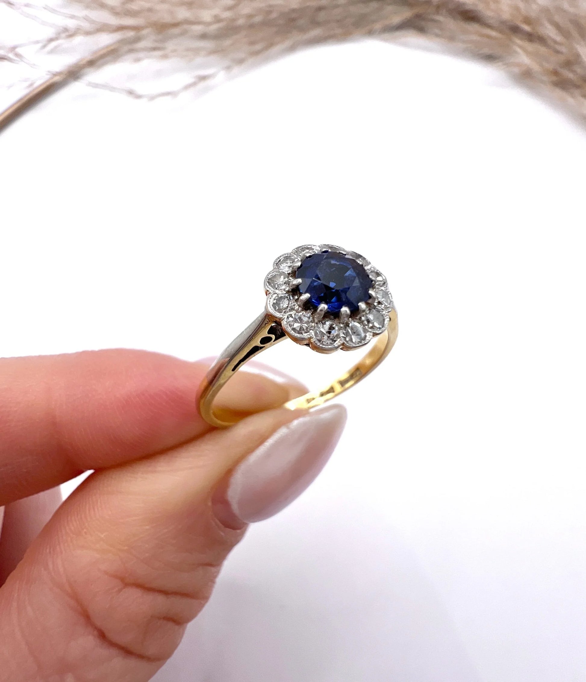 A sapphire and diamond flower cluster ring in yellow gold and platinum, held in a hand