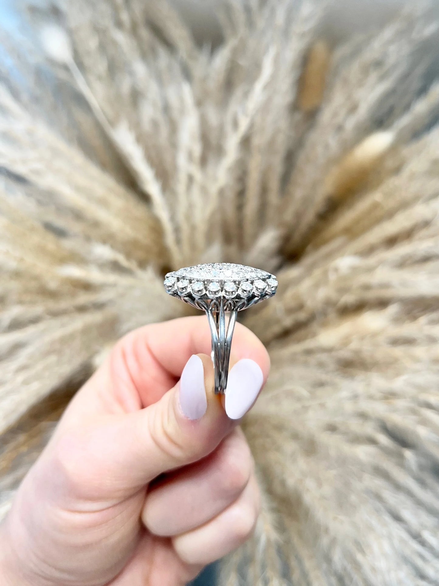 A navette shaped diamond cluster ring in white metal, held in a hand