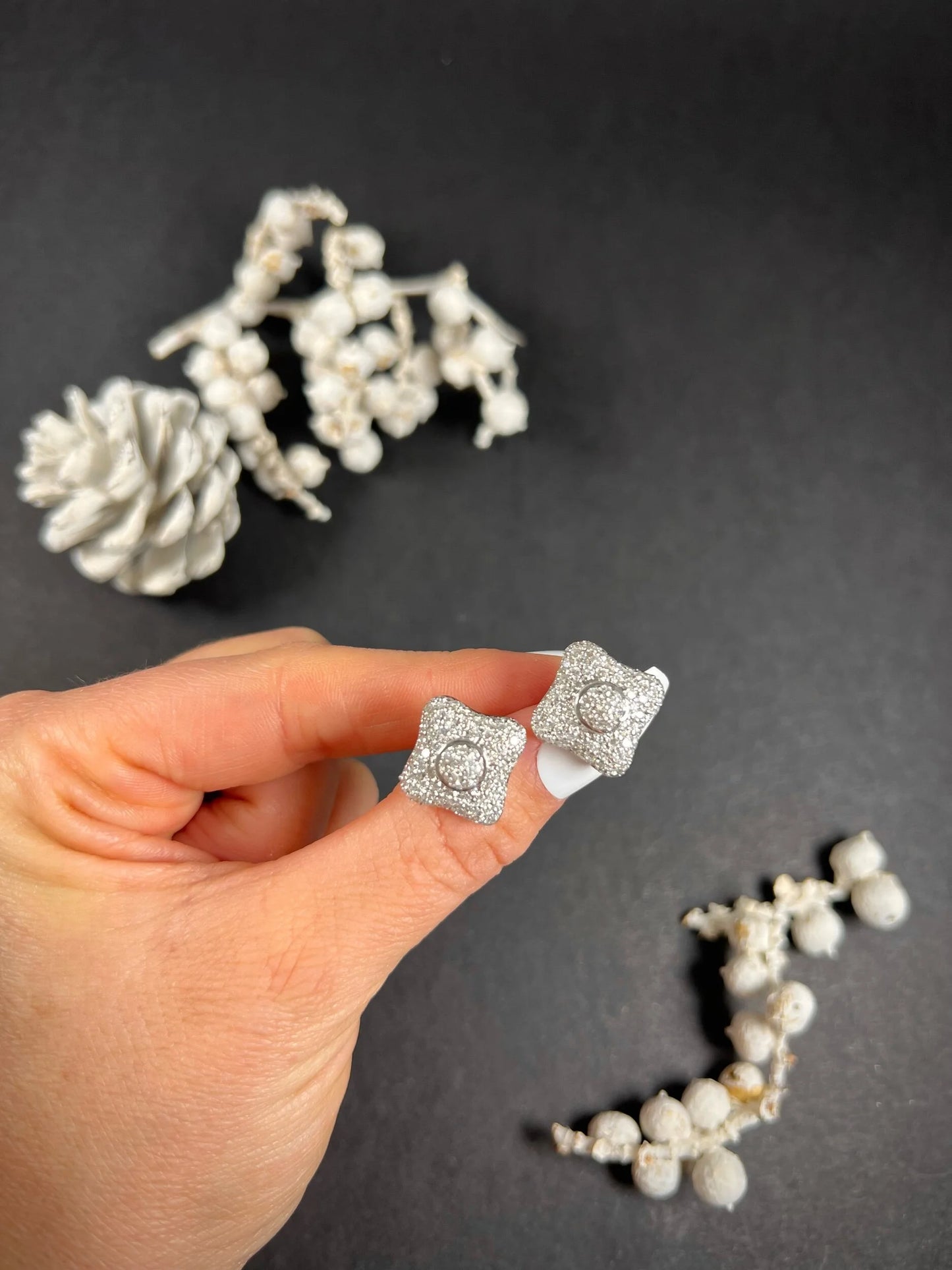 A pair of diamond cluster stud earrings in white gold, held in a hand
