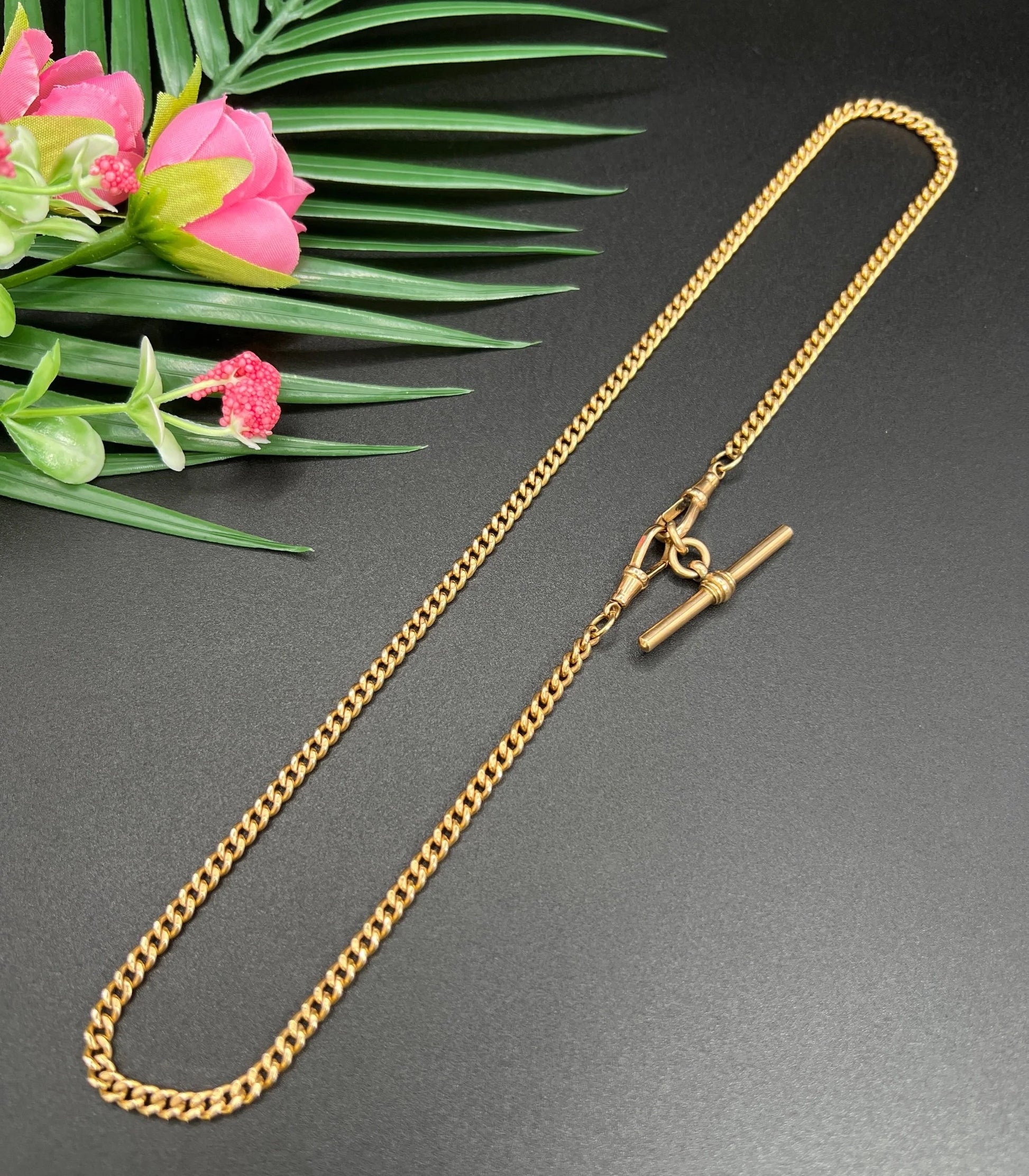 A gold curb link Albert chain, laid flat on a black background
