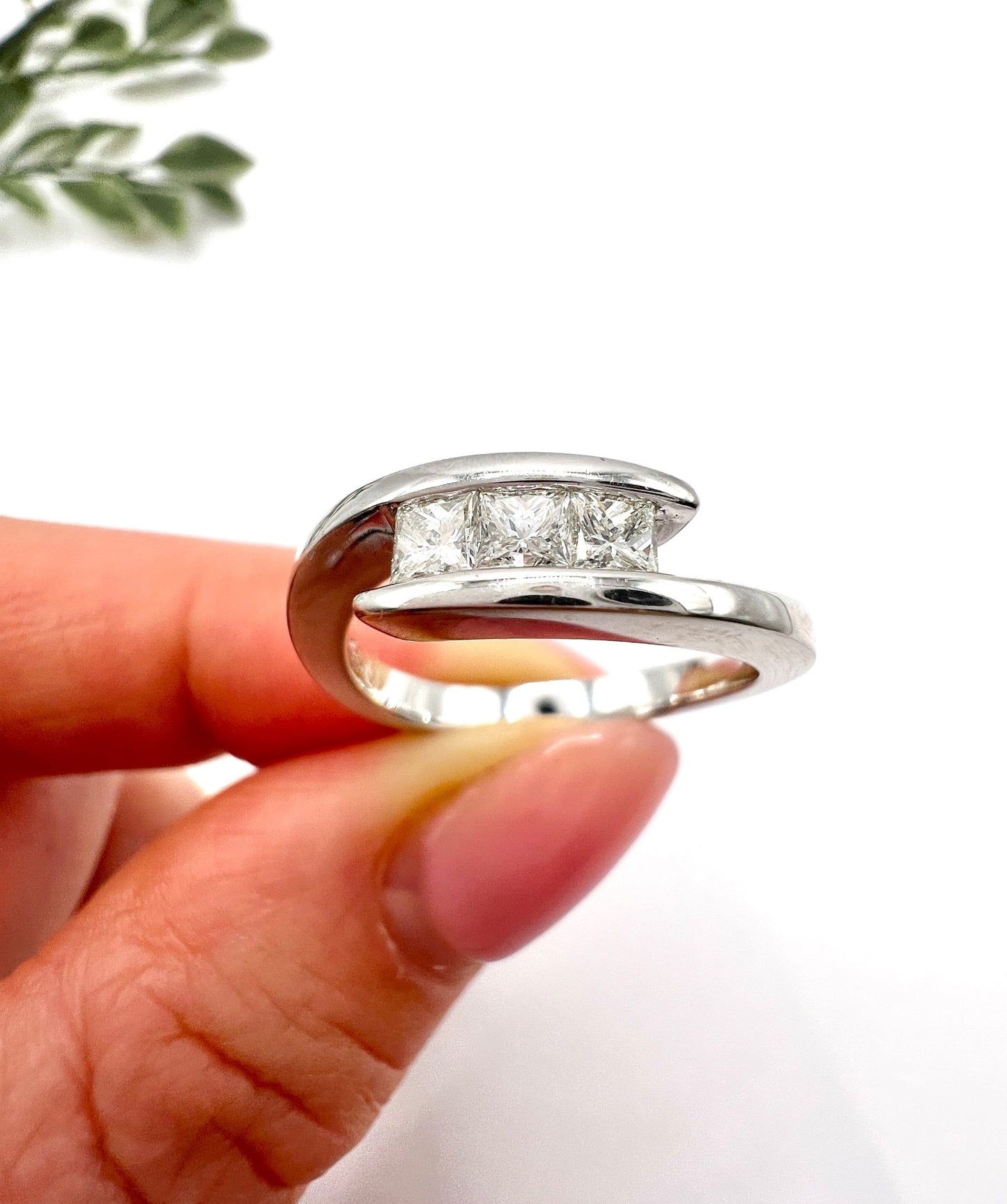 A three stone princess cut diamond crossover ring in white gold, held in a hand