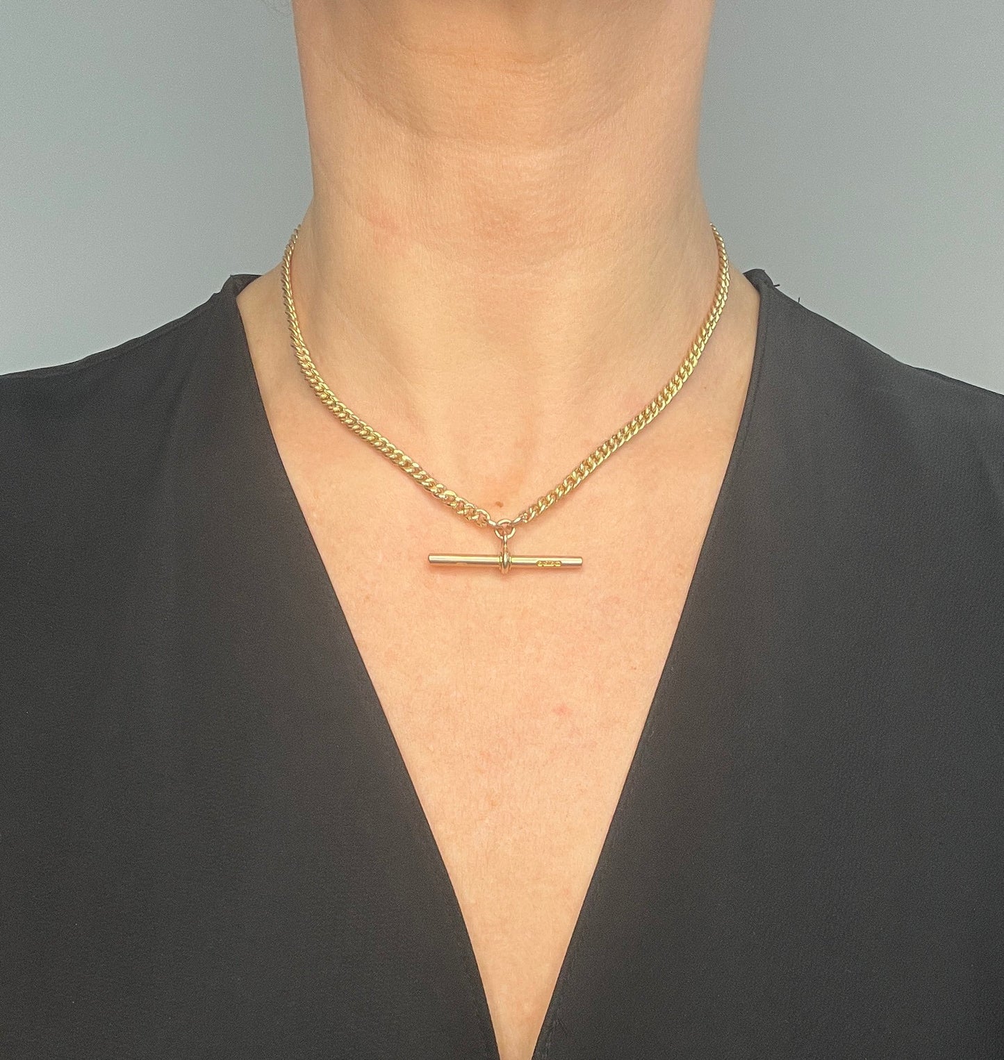 A yellow gold curb link Albert watch chain, modelled by a woman wearing a black top