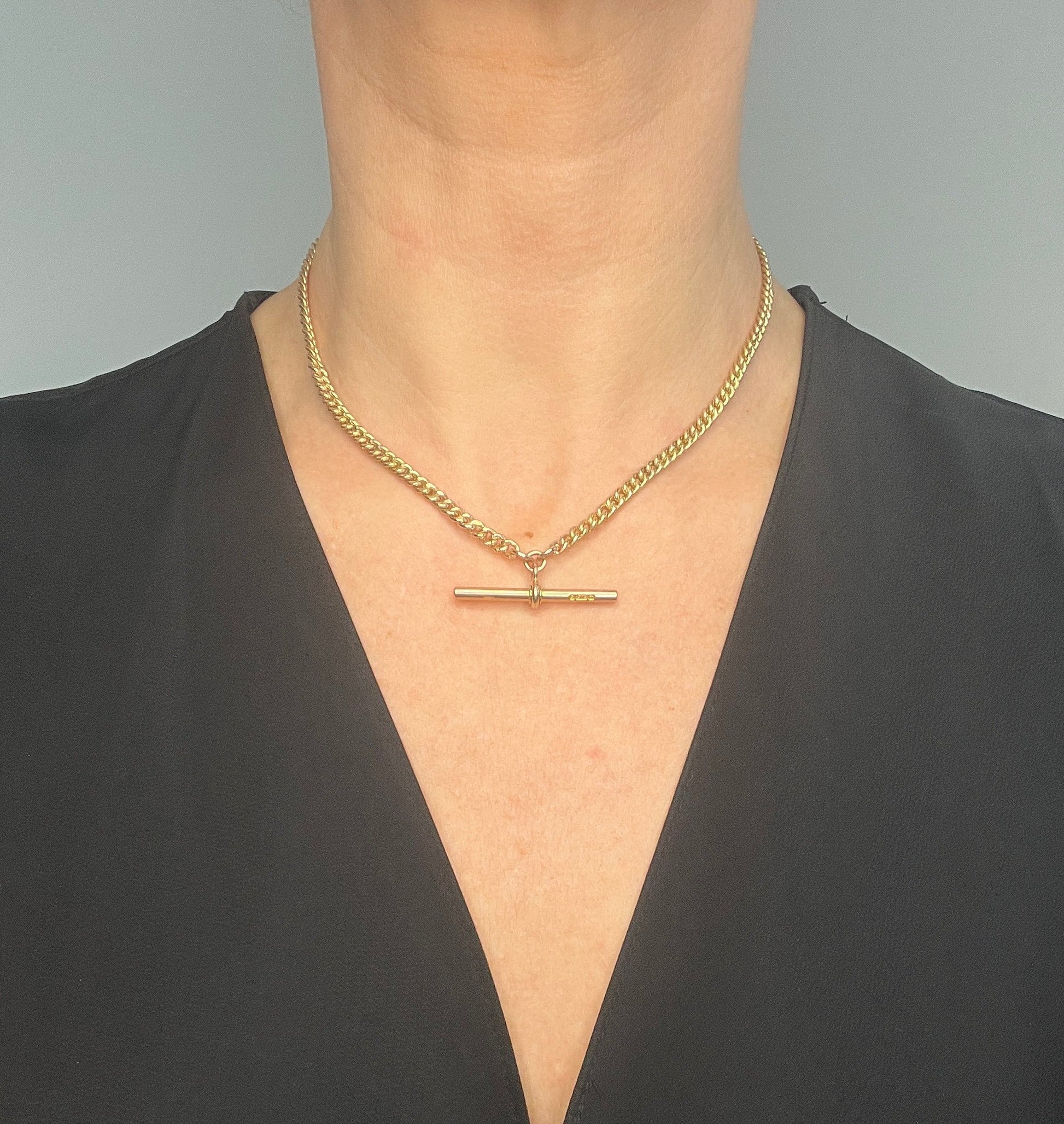 A yellow gold curb link Albert watch chain, modelled by a woman wearing a black top