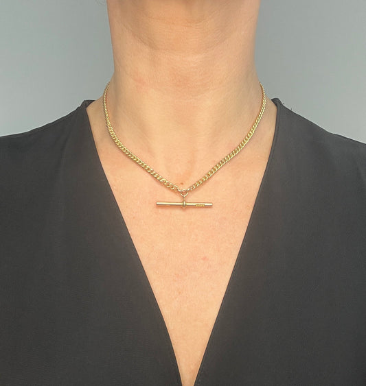 A yellow gold curb link Albert watch chain, modelled by a woman wearing a black top