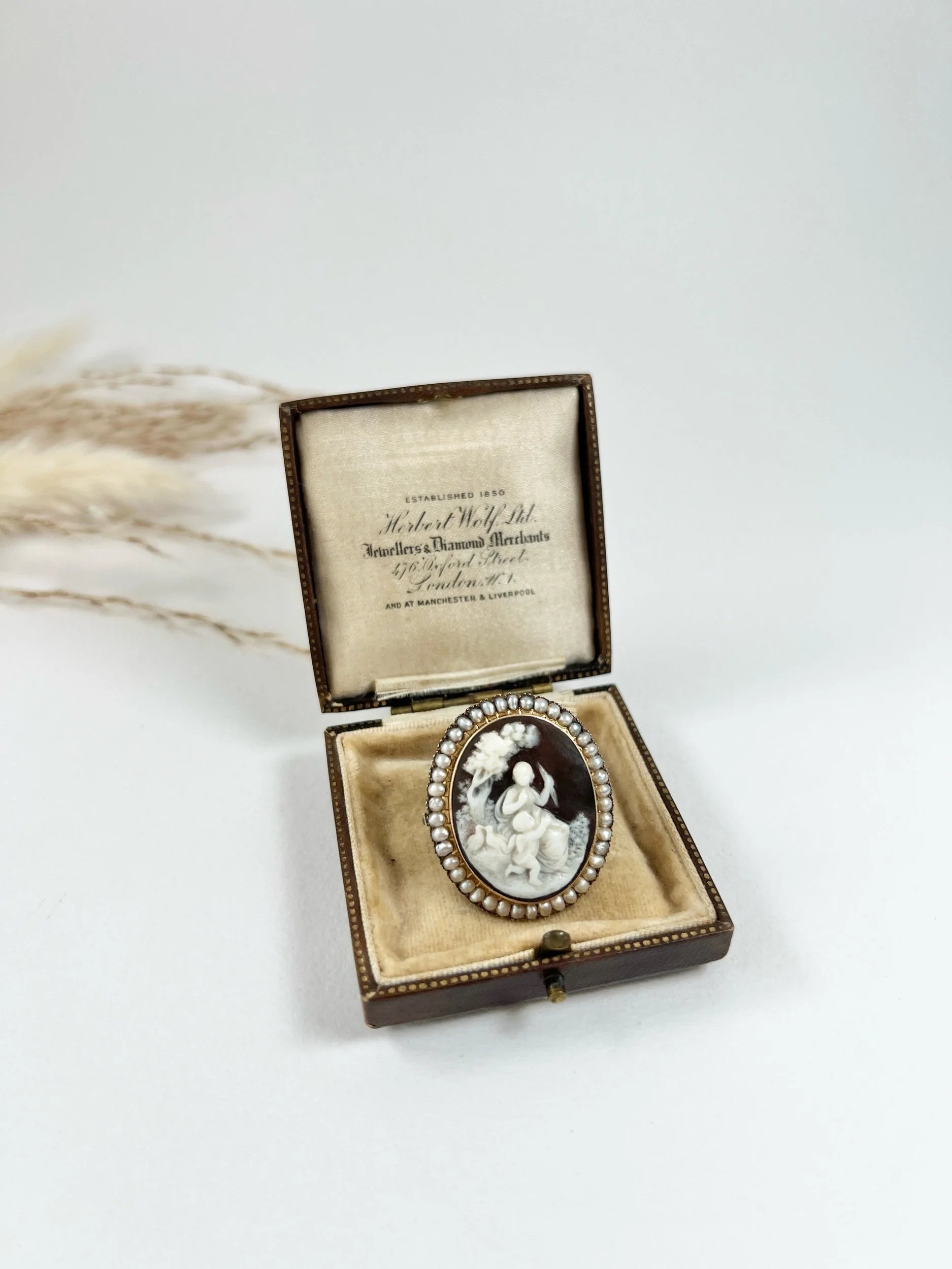 An antique oval cameo brooch depicting cherubs and birds, with a pearl border, set in gold