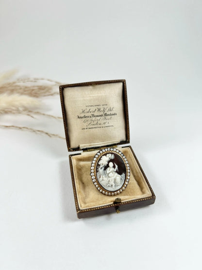 An antique oval cameo brooch depicting cherubs and birds, with a pearl border, set in gold