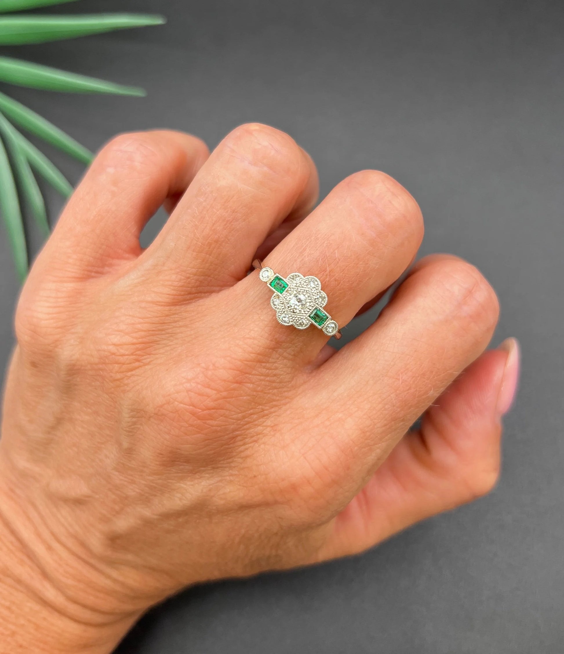 An emerald and diamond floral cluster ring in yellow gold and platinum, modelled on a hand