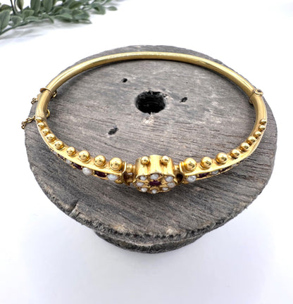 A yellow gold bangle bracelet set with rubies and seed pearls