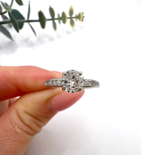 A solitaire diamond ring with diamond shoulders in platinum, held in a hand