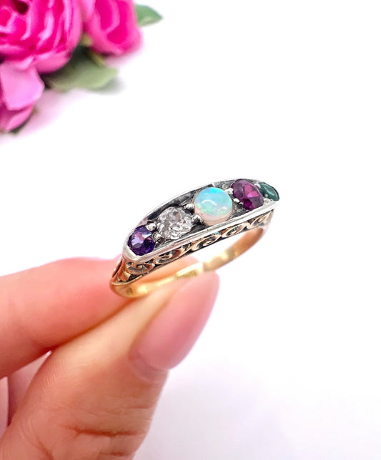 A yellow gold and platinum five stone ring set with amethyst, diamond, opal, ruby and emerald, held in a hand