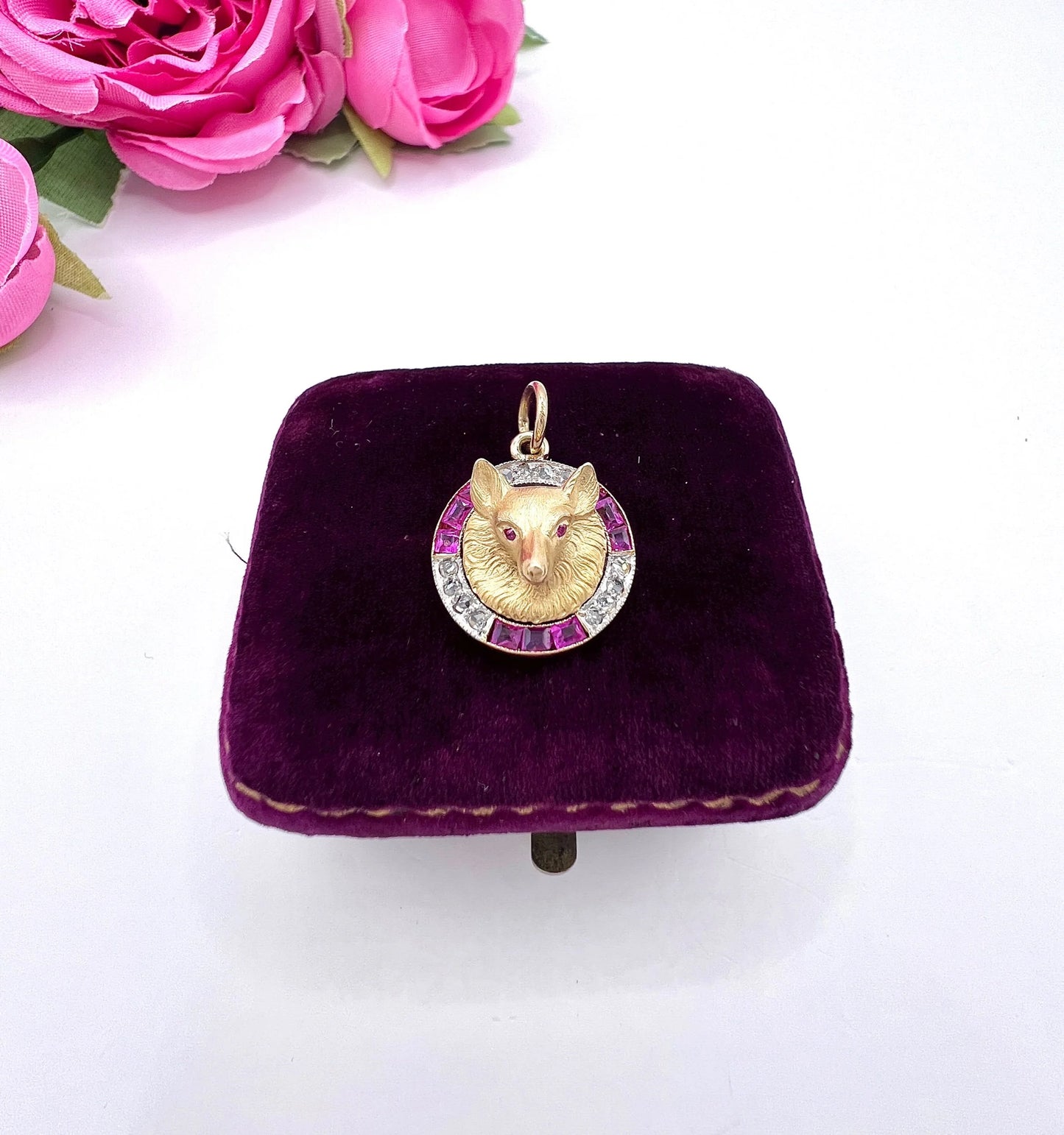 A fox head pendant in yellow gold with a ruby and diamond border