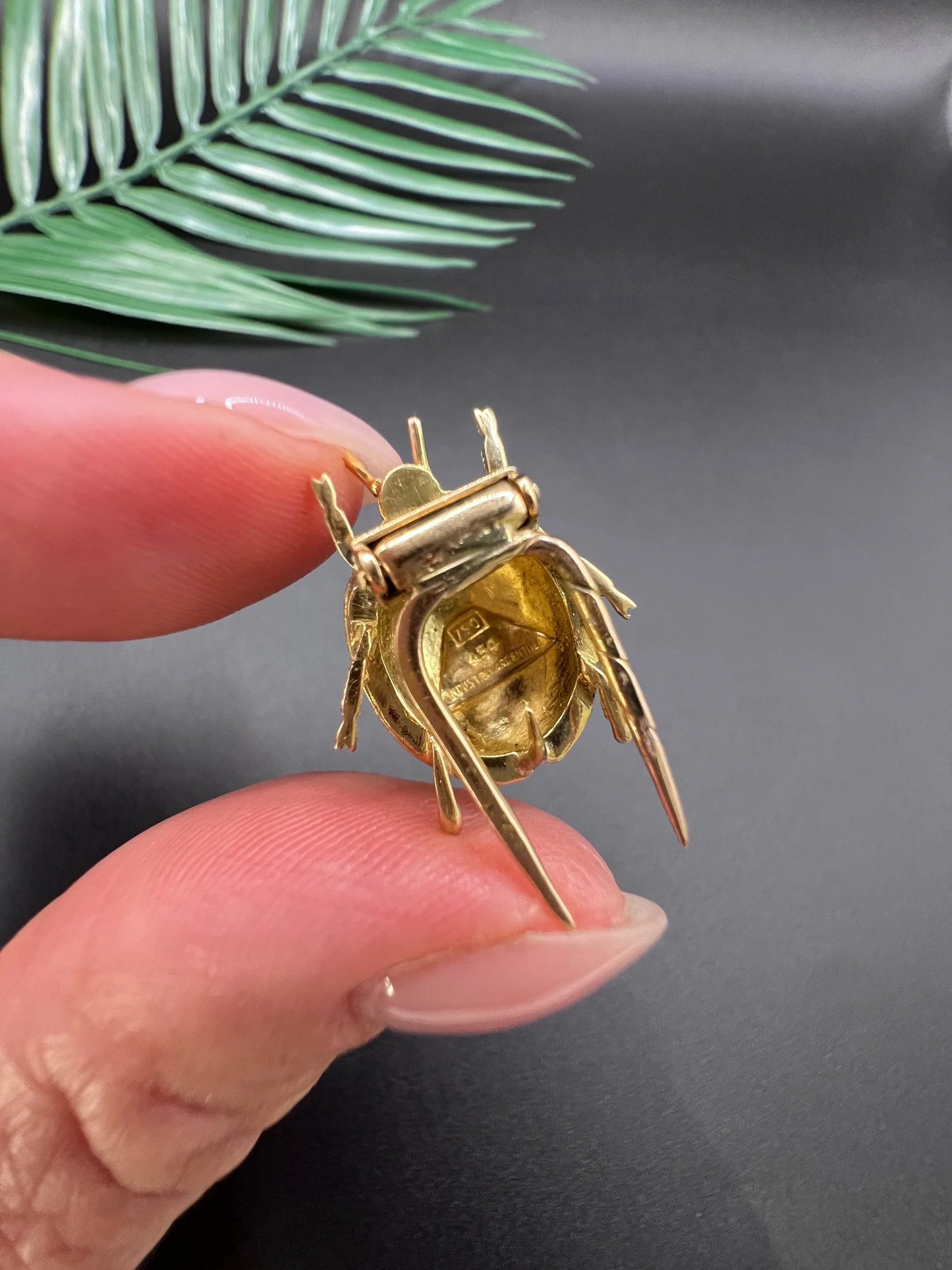 A yellow gold and enamel ladybird brooch, held in a hand
