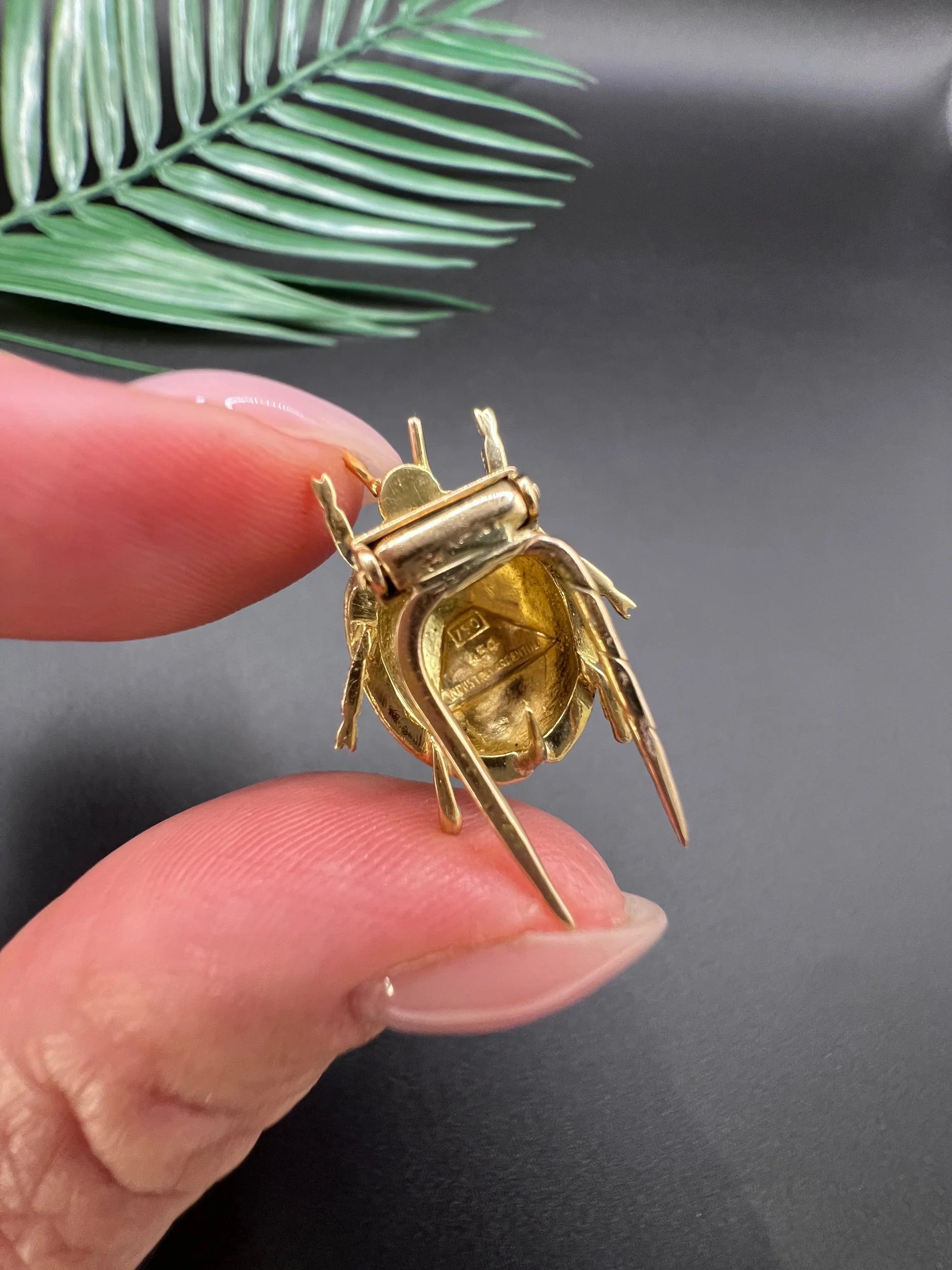 A yellow gold and enamel ladybird brooch, held in a hand