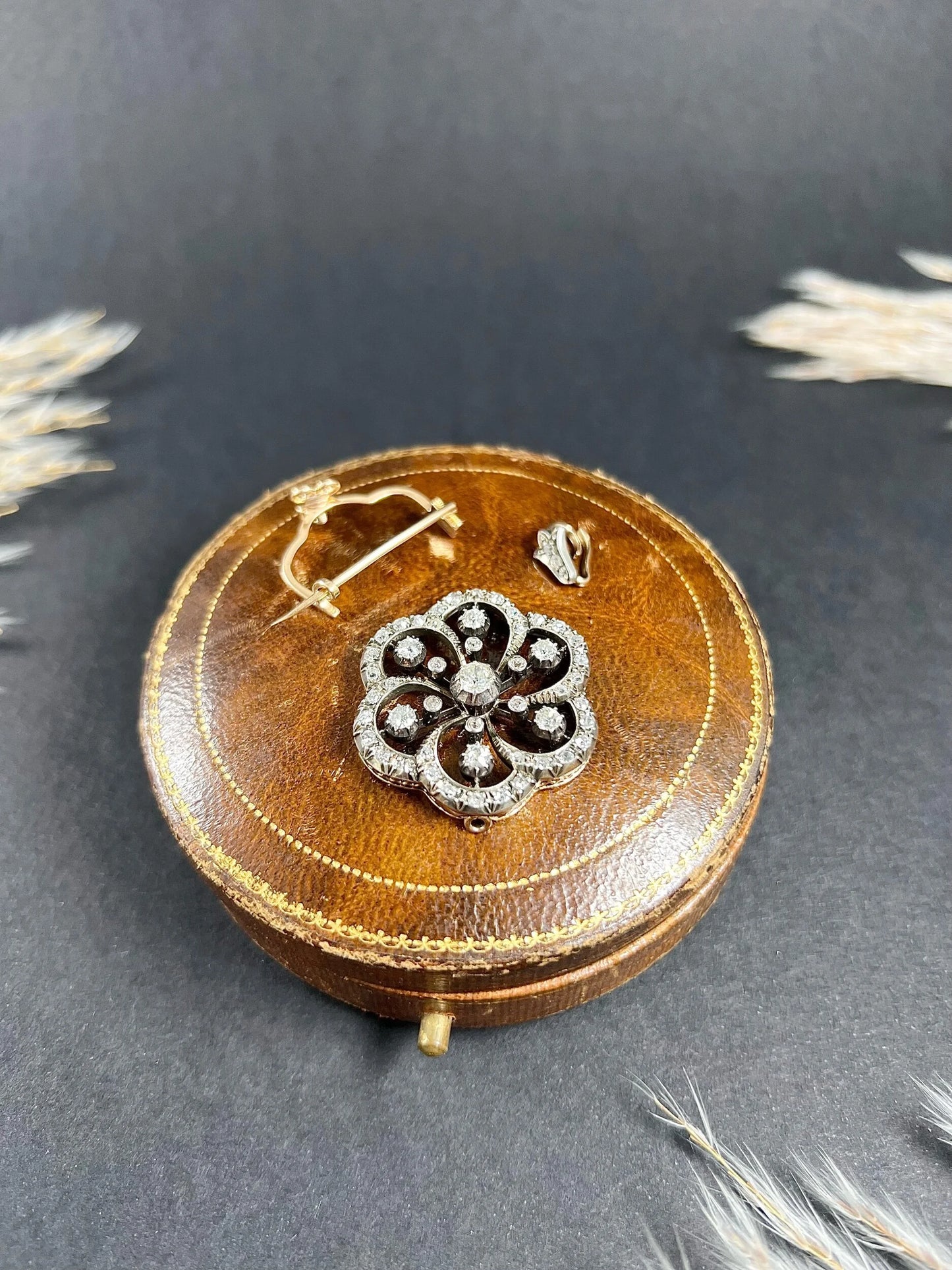 A floral design diamond set pendant/brooch on an antique brown jewellery box