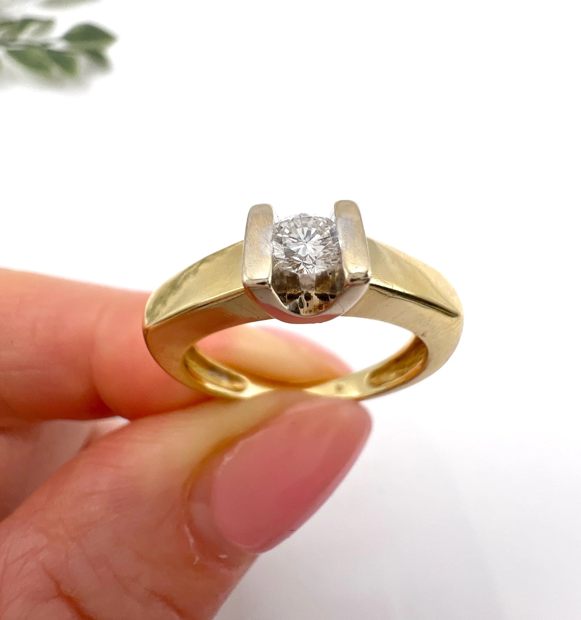 A brilliant cut diamond solitaire ring in yellow gold, held in a hand