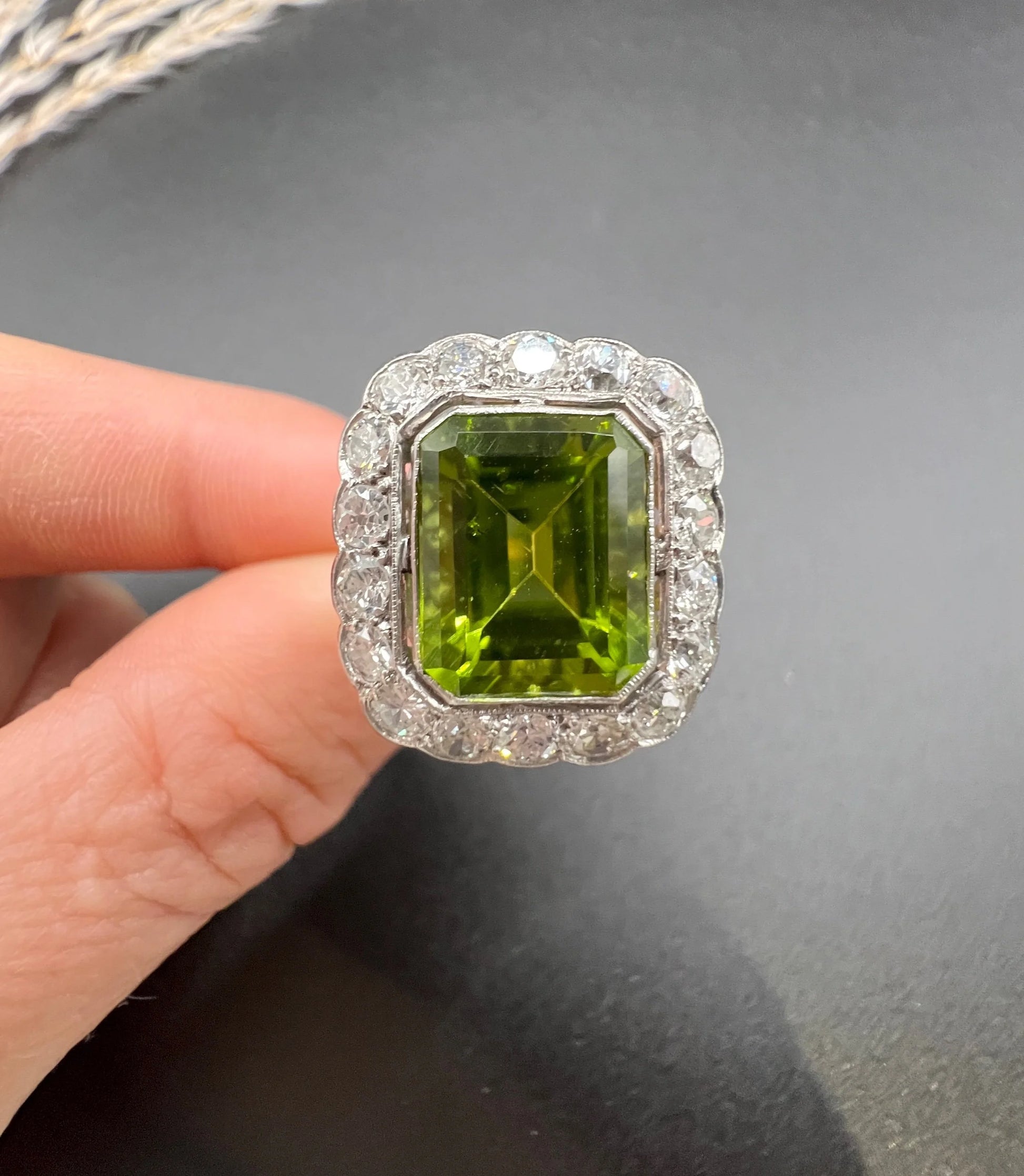 A cushion shaped peridot and diamond cluster ring in white metal, held in a hand
