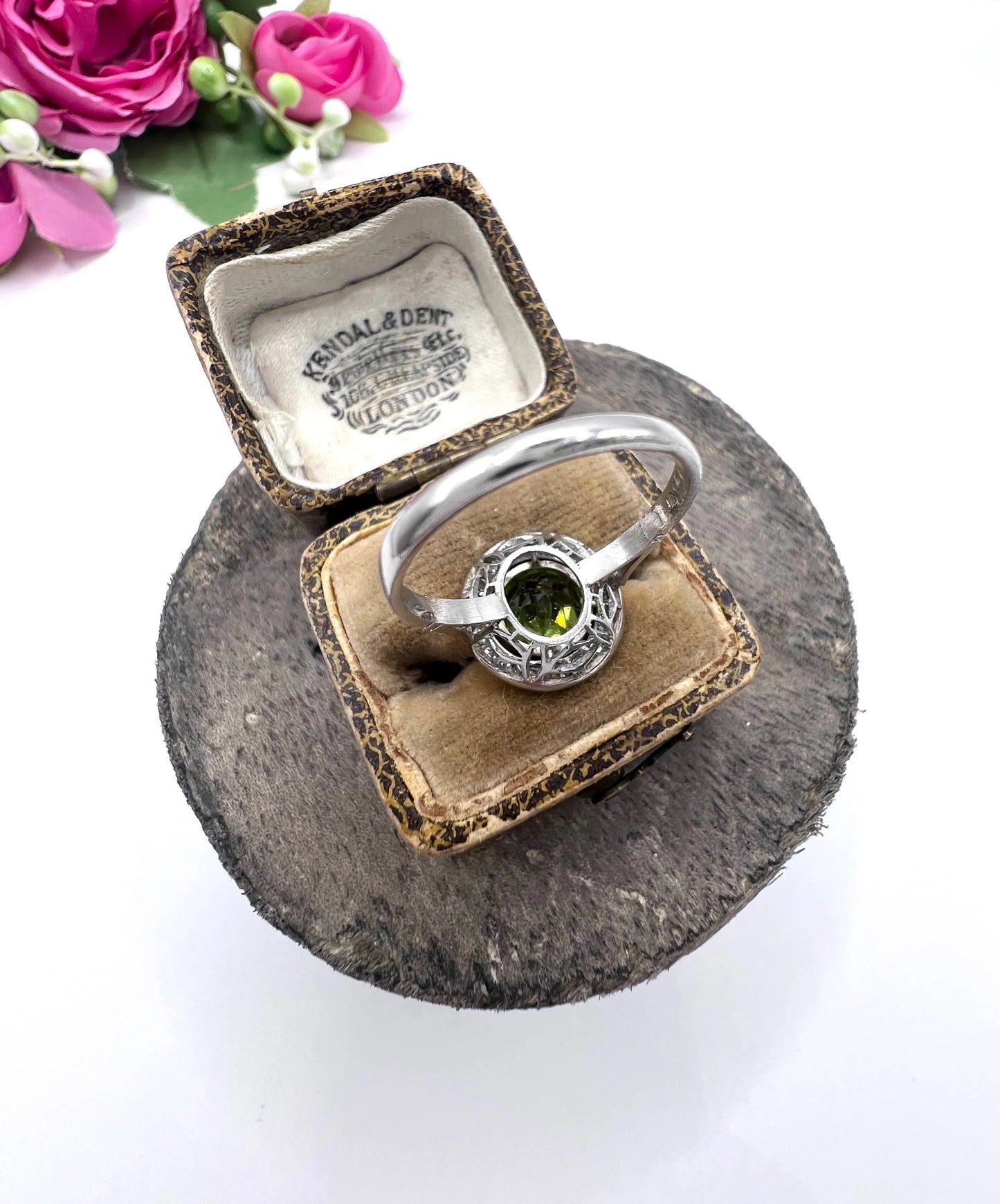 A white gold circular target cluster ring with a peridot centre surrounded by diamonds, in a ring box