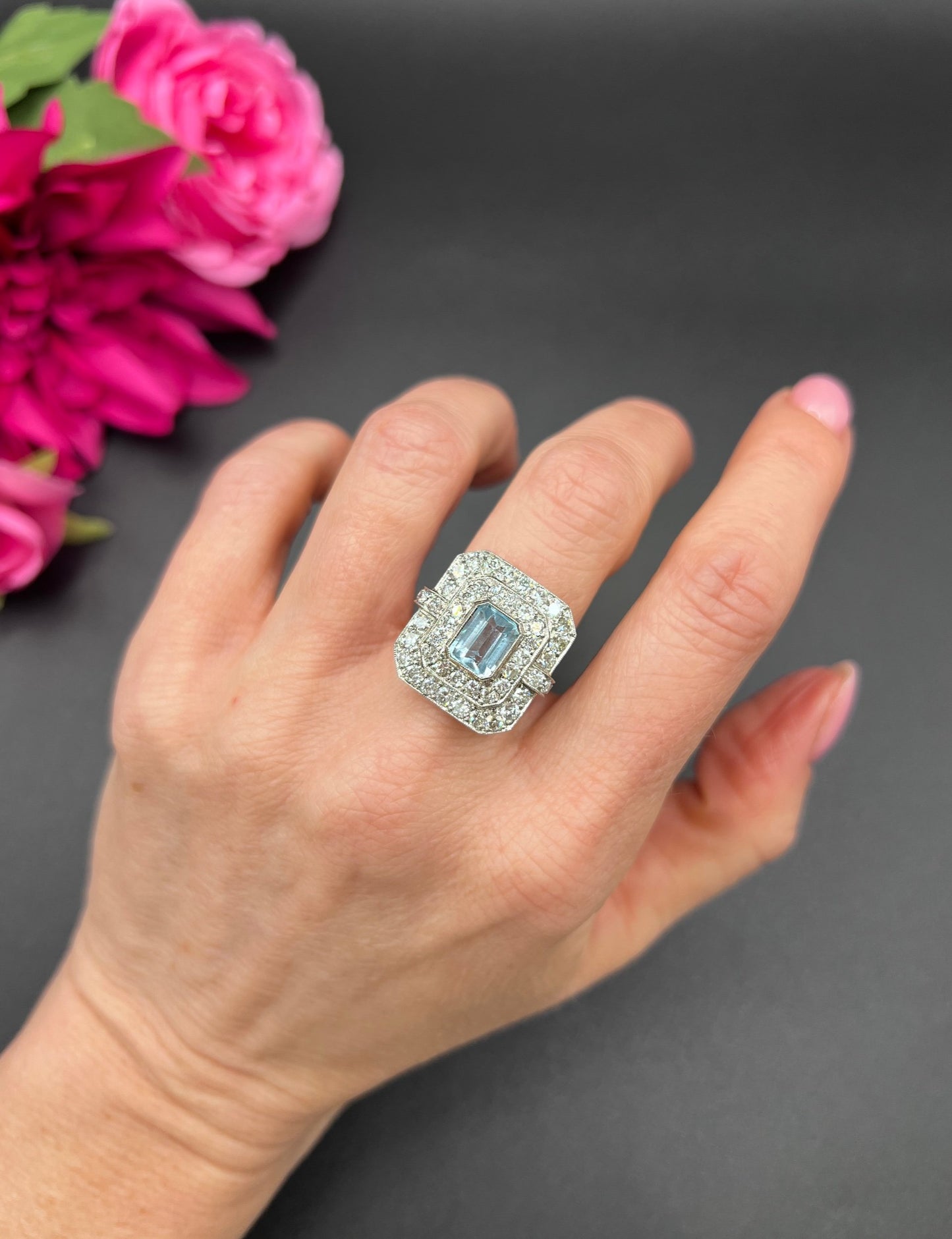 An octagonal shaped cluster ring with an aquamarine centre surrounded by two rows of diamonds, in platinum, modelled on a hand