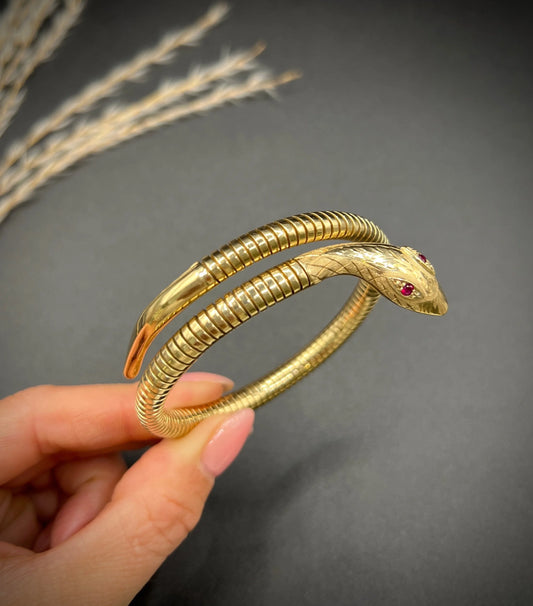 A yellow gold snake bracelet with ruby eyes, held in a hand