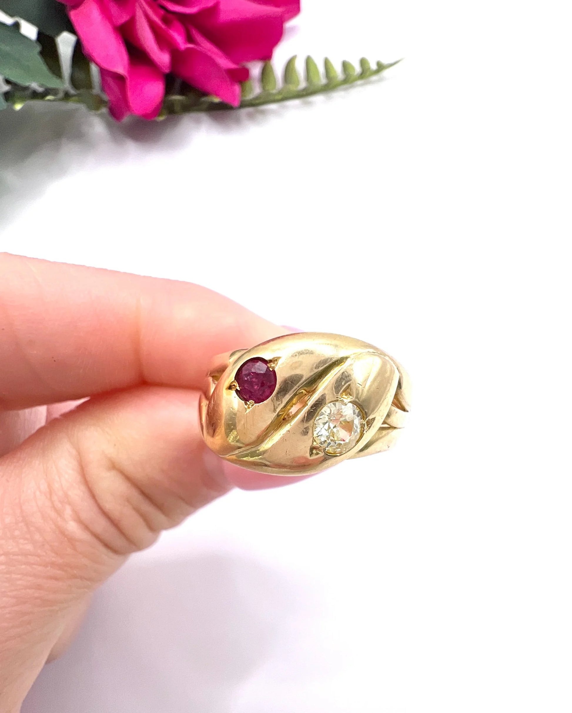 A yellow gold double headed snake ring with a ruby and a diamond, held in a hand