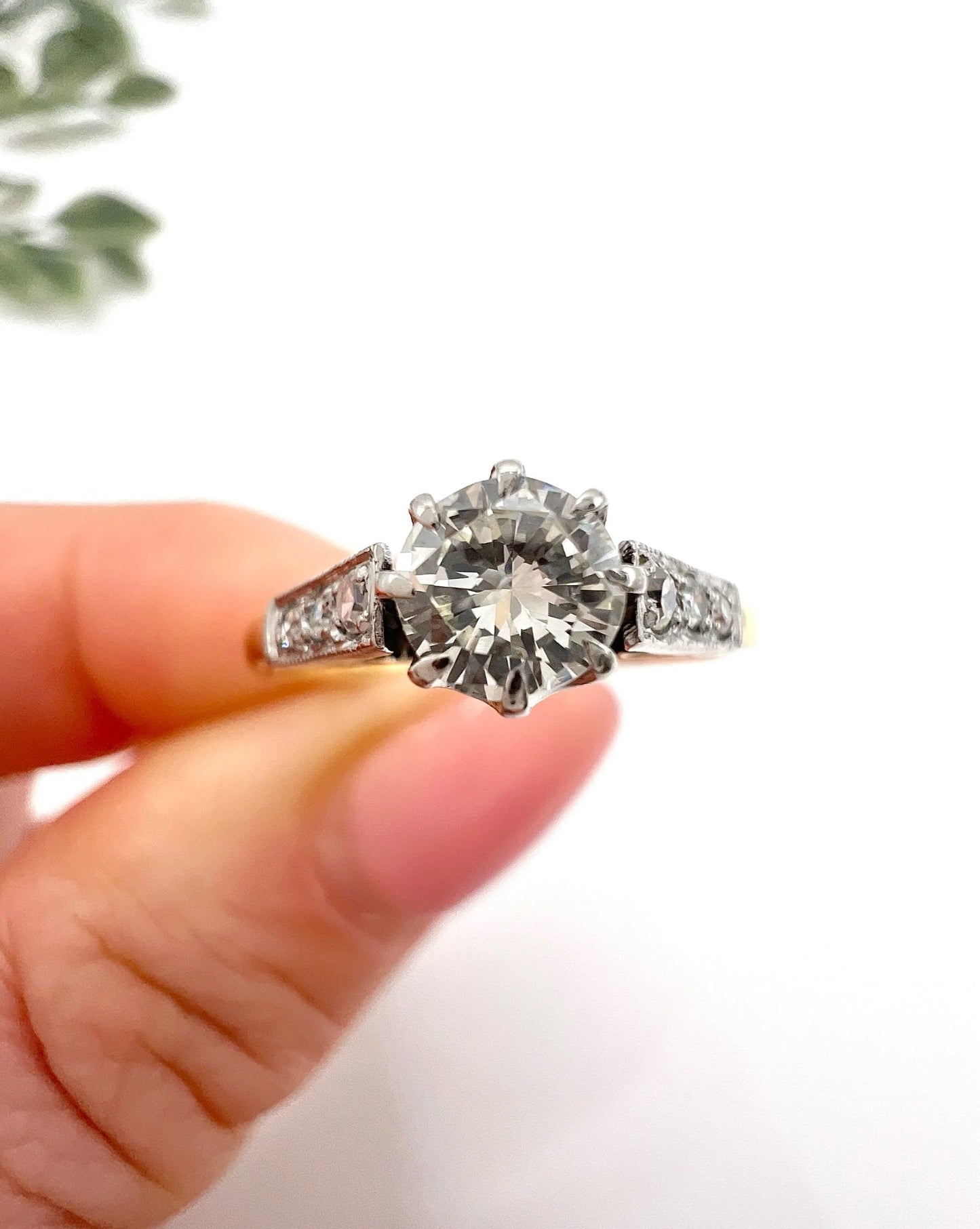 A diamond engagement style ring in yellow gold and platinum, held in a hand