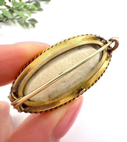 An oval yellow gold brooch with a locket compartment, held in a hand