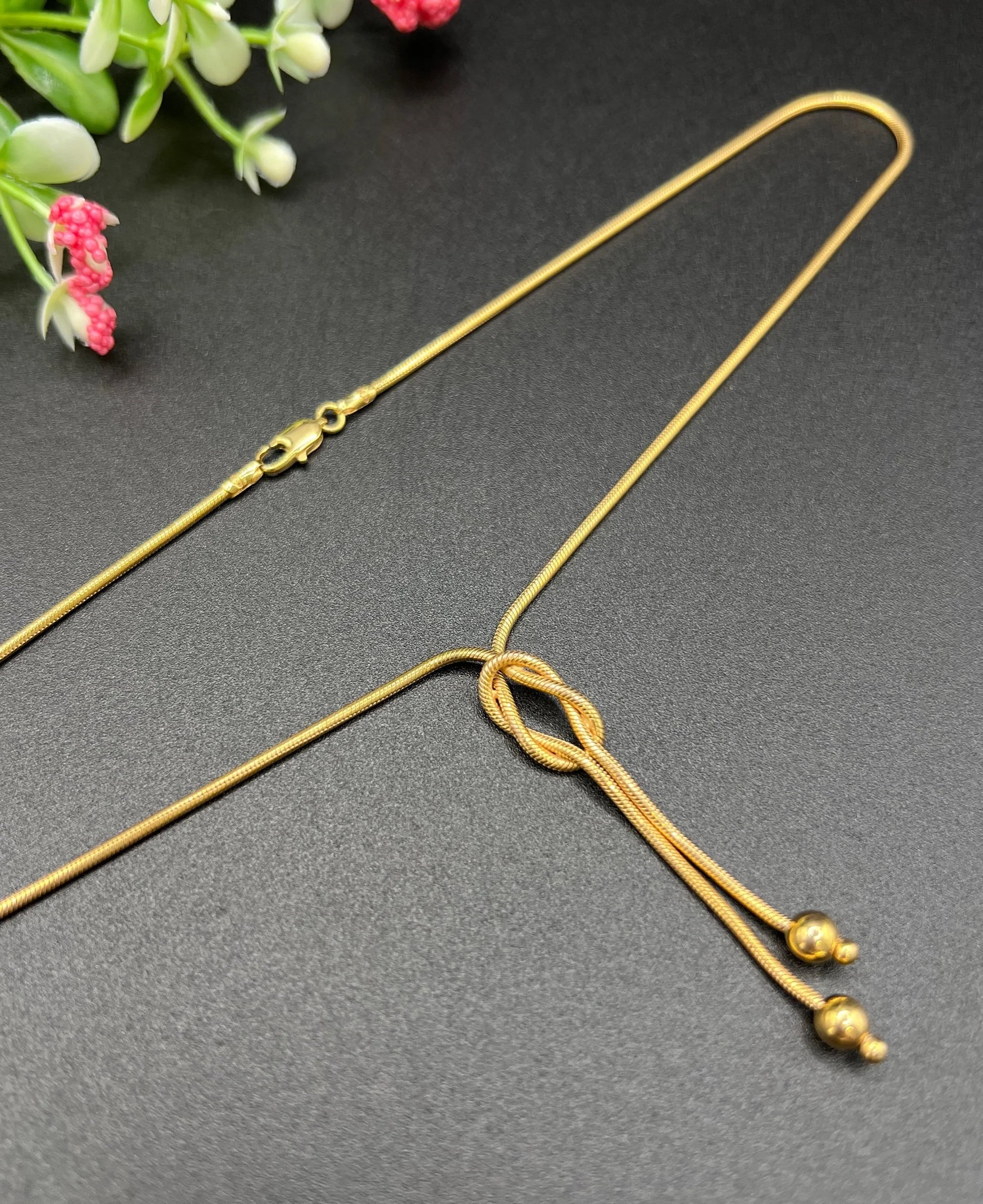 A yellow gold snake link chain necklace with a knot and tassel drop