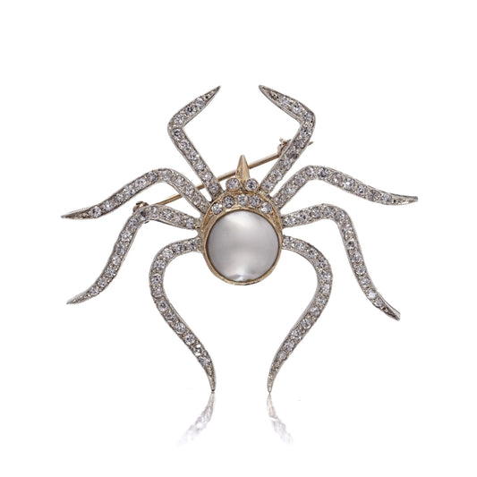 A spider brooch set with a pearl and diamonds, in gold and silver, on a white background