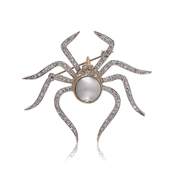 A spider brooch set with a pearl and diamonds, in gold and silver, on a white background