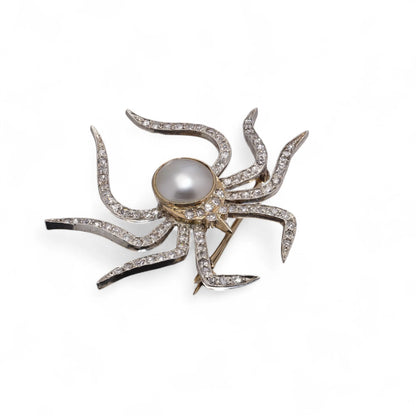 A spider brooch set with a pearl and diamonds, in gold and silver, on a white background