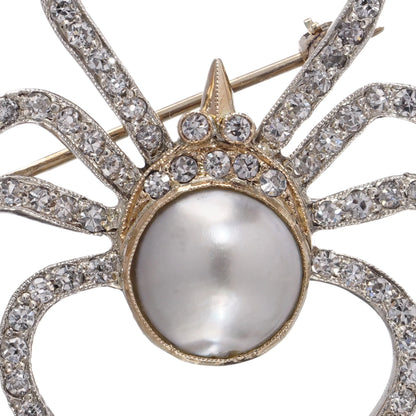 A spider brooch set with a pearl and diamonds, in gold and silver, on a white background