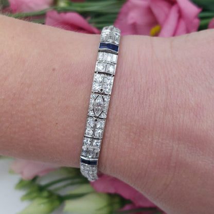 An Art Deco line bracelet set with four marquise cut diamonds to an encrusted border of early brilliant cut and baguette cut diamonds with sapphire accents. These bright, white diamonds are estimated to weigh a total of 4.80ct.