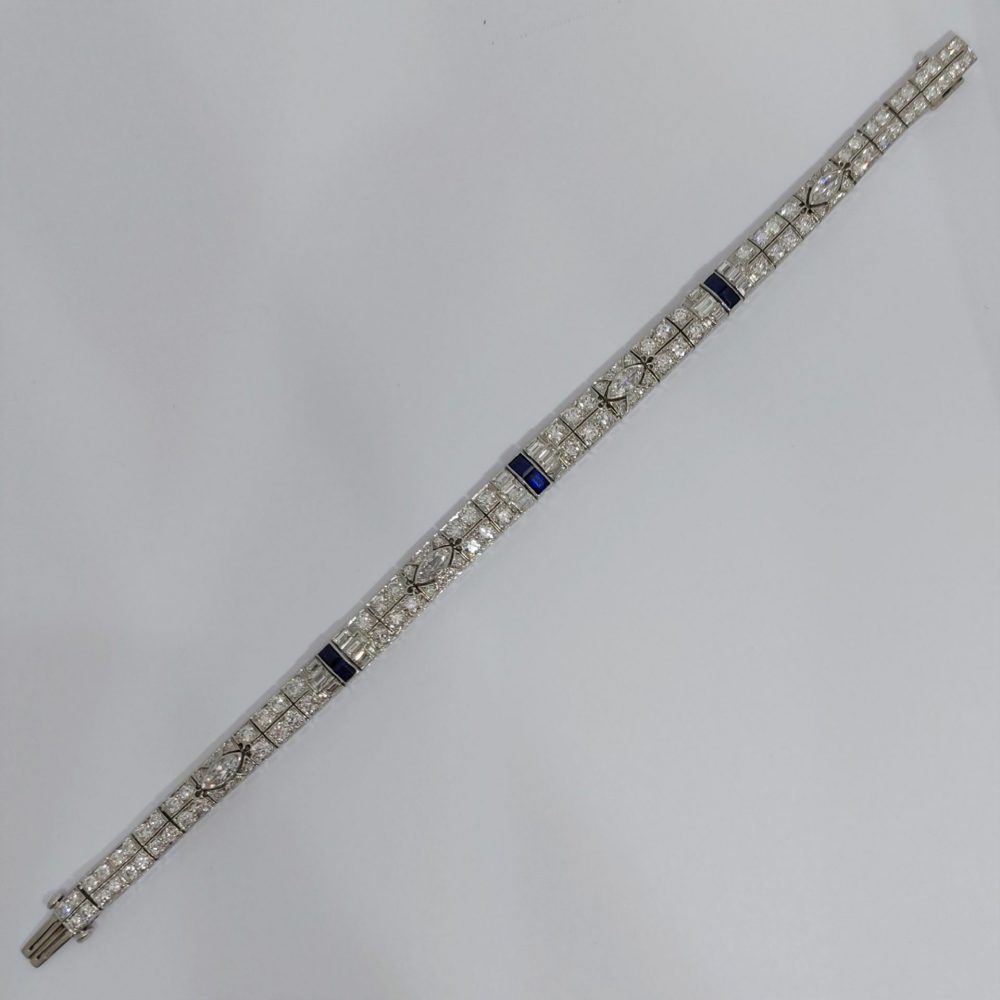 An Art Deco line bracelet set with four marquise cut diamonds to an encrusted border of early brilliant cut and baguette cut diamonds with sapphire accents. These bright, white diamonds are estimated to weigh a total of 4.80ct.