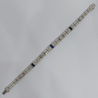 An Art Deco line bracelet set with four marquise cut diamonds to an encrusted border of early brilliant cut and baguette cut diamonds with sapphire accents. These bright, white diamonds are estimated to weigh a total of 4.80ct.
