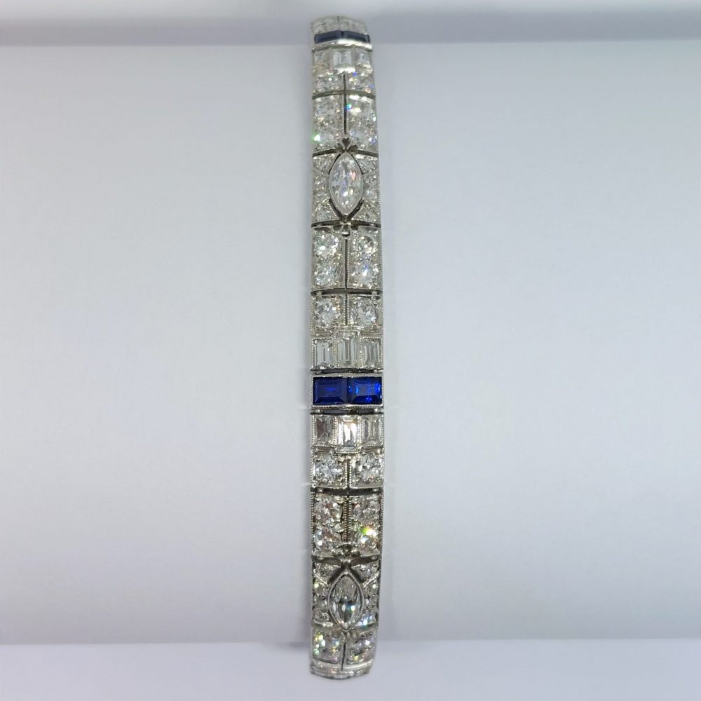An Art Deco line bracelet set with four marquise cut diamonds to an encrusted border of early brilliant cut and baguette cut diamonds with sapphire accents. These bright, white diamonds are estimated to weigh a total of 4.80ct.