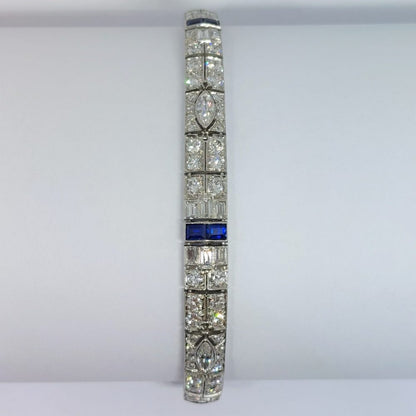An Art Deco line bracelet set with four marquise cut diamonds to an encrusted border of early brilliant cut and baguette cut diamonds with sapphire accents. These bright, white diamonds are estimated to weigh a total of 4.80ct.