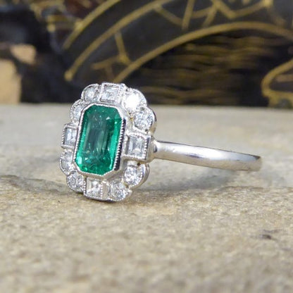 A beautiful contemporary ring featuring a 0.50ct emerald cut emerald with a diamond surround. With princess and modern brilliant cut diamonds alternating around the emerald, this ring has a total of 0.35ct diamonds allowing it to sparkle beautifully on the finger all set in platinum in a millegrain edge.