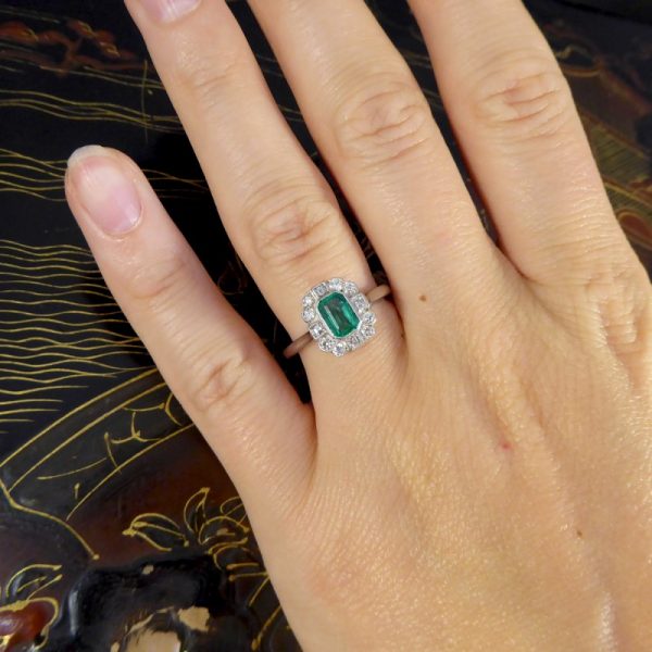 A beautiful contemporary ring featuring a 0.50ct emerald cut emerald with a diamond surround. With princess and modern brilliant cut diamonds alternating around the emerald, this ring has a total of 0.35ct diamonds allowing it to sparkle beautifully on the finger all set in platinum in a millegrain edge.