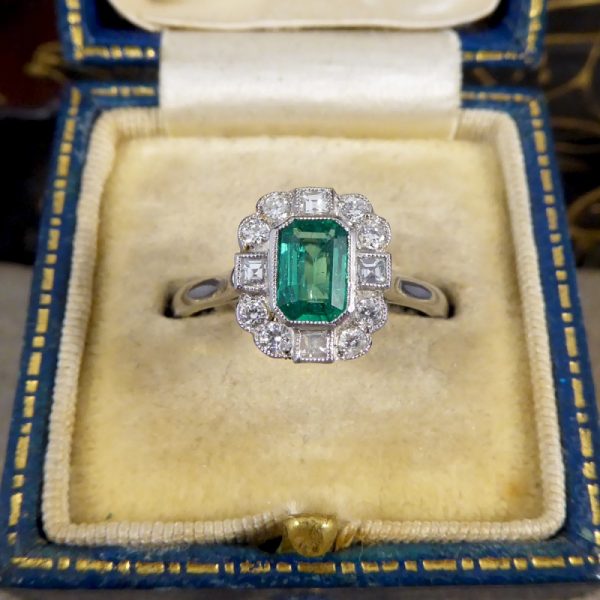 A beautiful contemporary ring featuring a 0.50ct emerald cut emerald with a diamond surround. With princess and modern brilliant cut diamonds alternating around the emerald, this ring has a total of 0.35ct diamonds allowing it to sparkle beautifully on the finger all set in platinum in a millegrain edge.