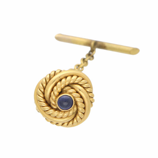 A yellow gold knot design tie tack with a blue sapphire, on a white background