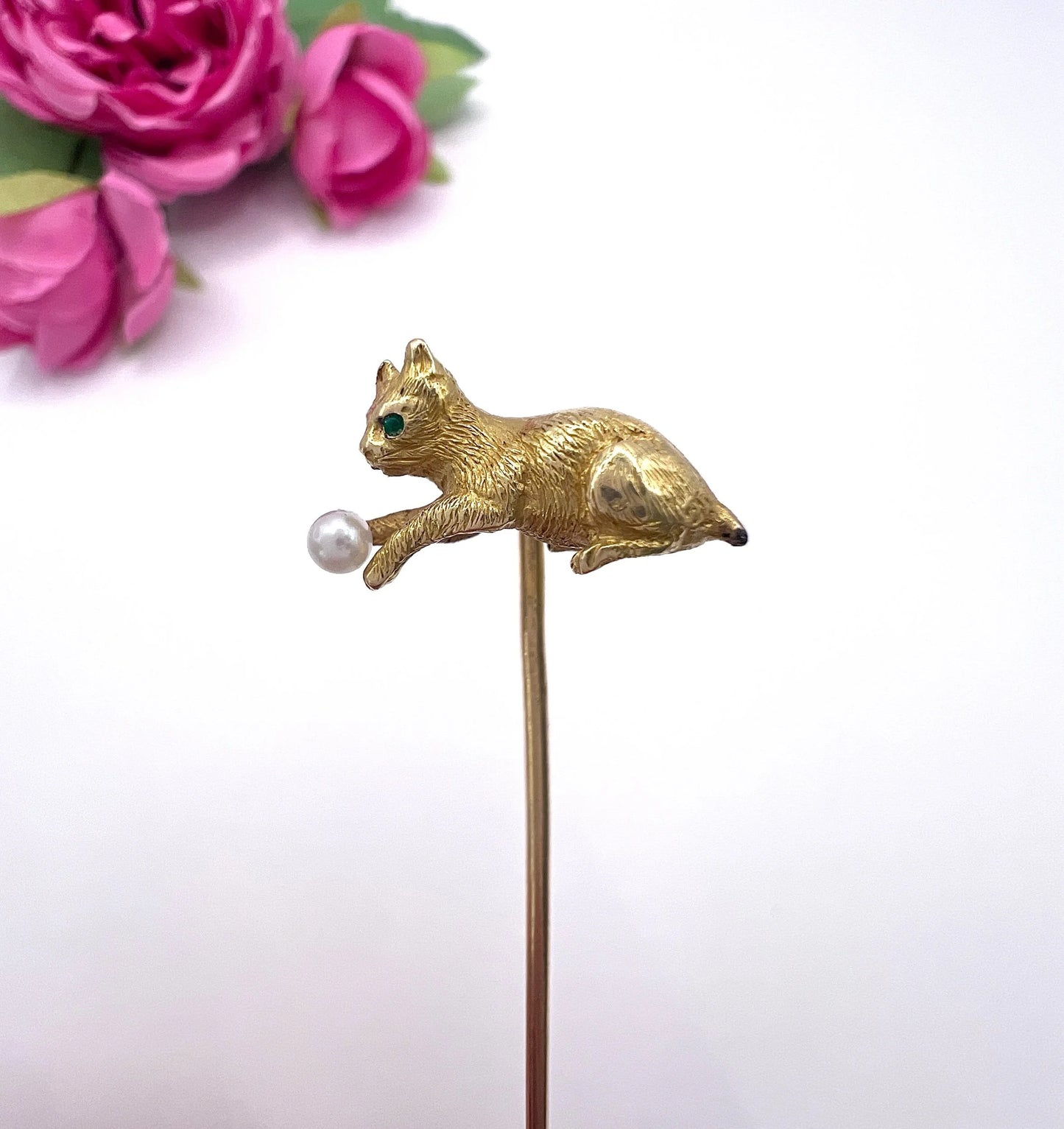 A yellow gold cat playing with a pearl ball stick pin