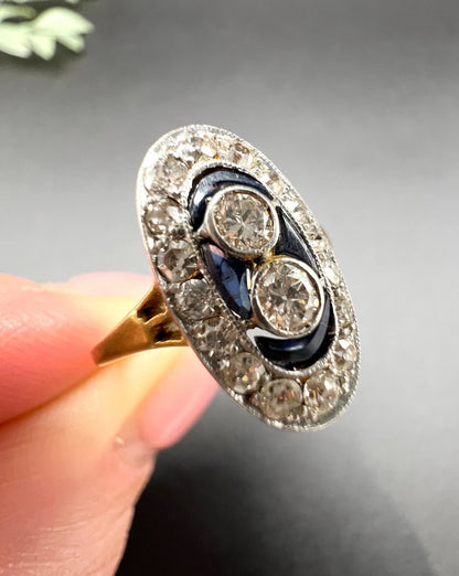 An oval cluster ring with diamonds and sapphires in platinum and yellow gold, held in a hand