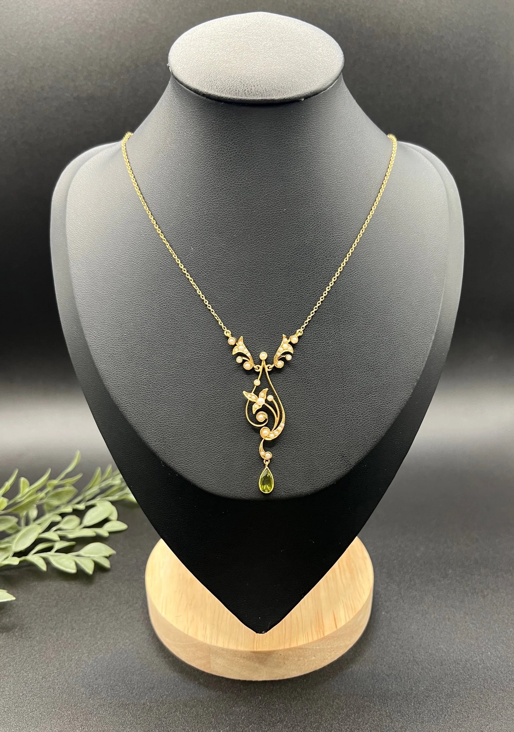 A yellow gold floral pendant necklace with pearls and a peridot drop, on a black jewellery bust