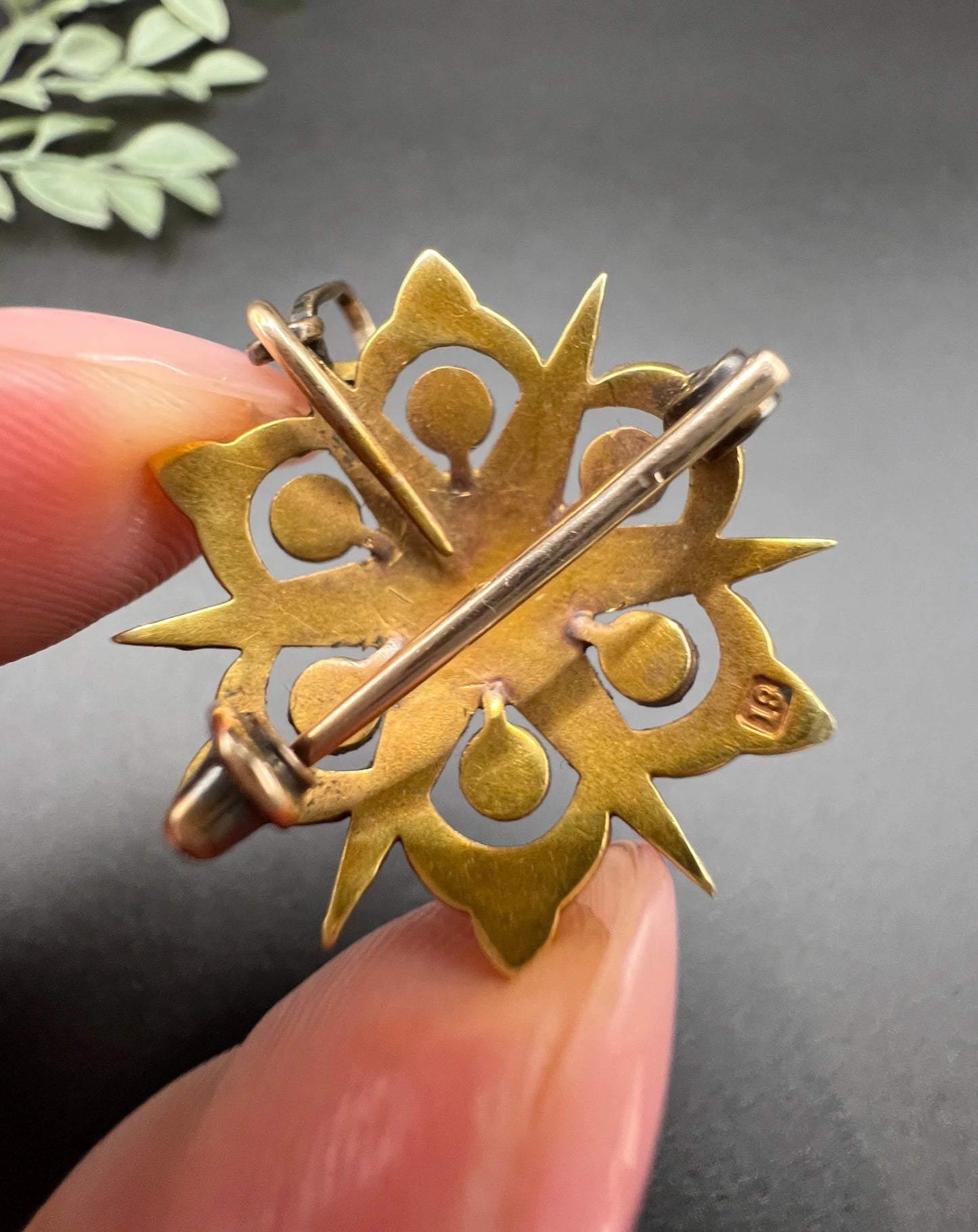 A yellow gold brooch/pendant with pearls in the shape of a star, held in a hand, stamped 18